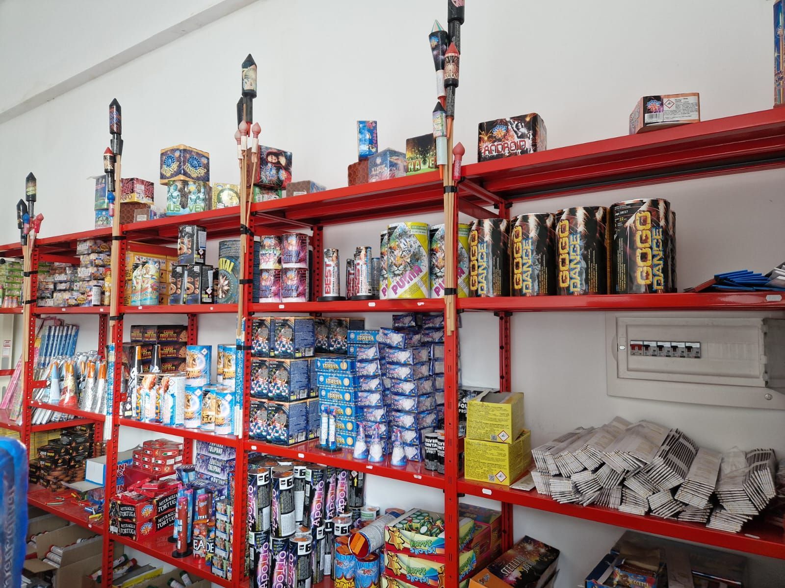 Scaffali metallici rossi in un corridoio di un magazzino, pieni di merci confezionate di vario genere e articoli piegati.