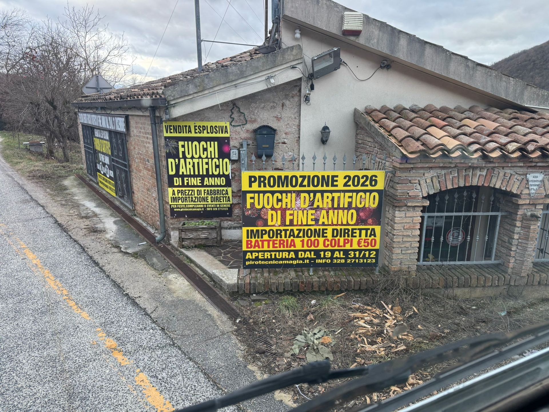 Muro a bordo strada con insegne promozionali italiane giallo-verdi su una casa rurale vicino a una strada bagnata