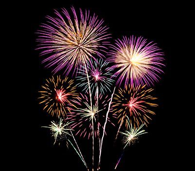 Fuochi d'artificio colorati che esplodono nel cielo notturno, con scintille rosa, dorate, rosse e bianche.
