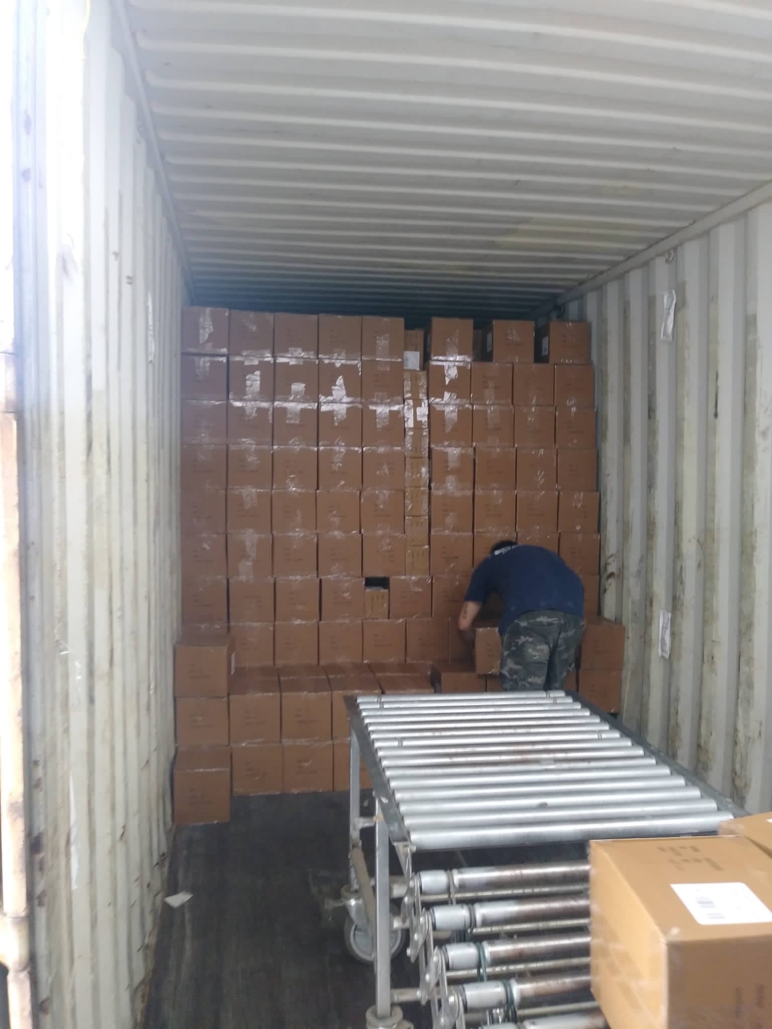 Man loading cardboard boxes into a shipping container using a conveyor belt.