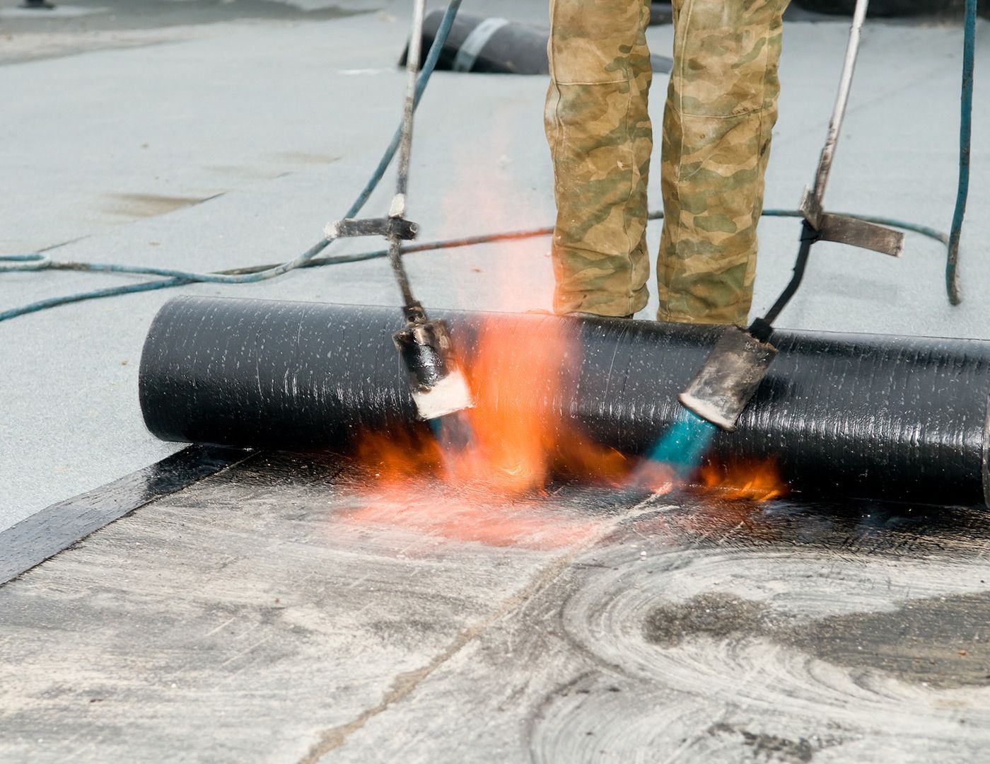 A person is using a torch to burn a roll of roofing material.