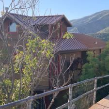 A large house with a metal roof is surrounded by trees and mountains.
