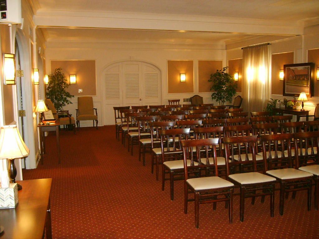 Interior of a room with rows of wooden chairs facing a closed white door.