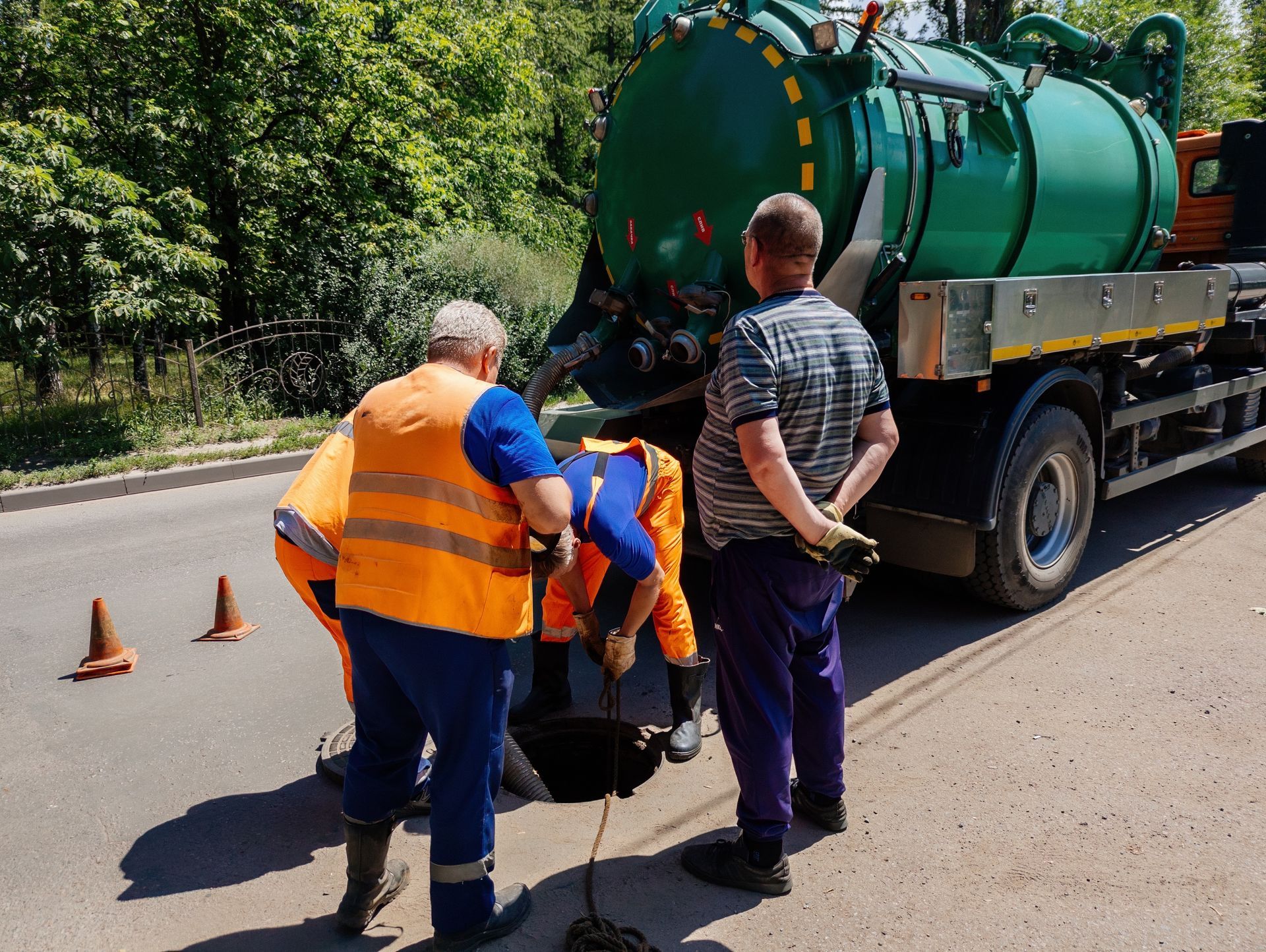 Utility crew inspecting a manhole beside a vacuum sewer service truck. Utility crew inspecting a manhole beside a vacuum sewer service truck.