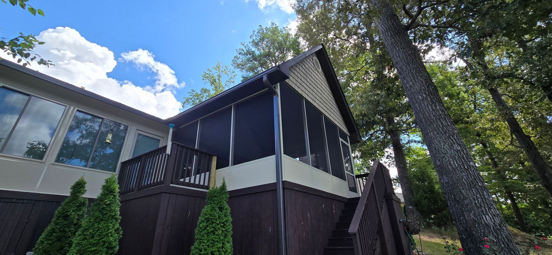 A cabin with a screened porch and large windows sits under a bright blue sky, surrounded by trees.