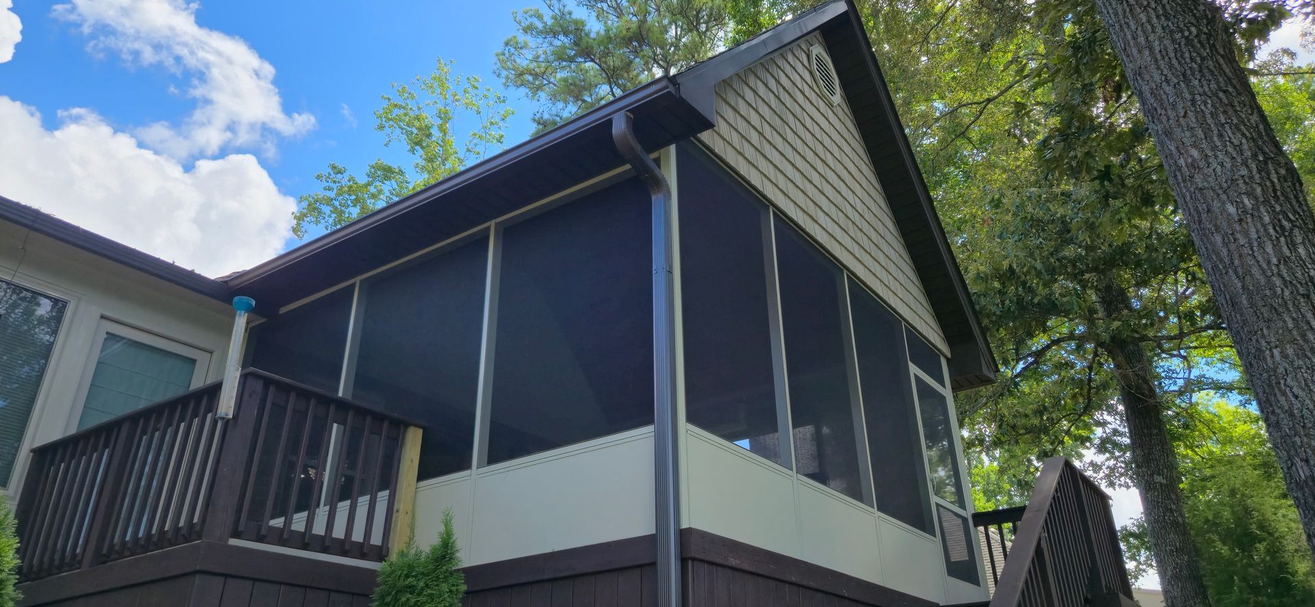 Screened porch with dark trim and siding, deck, and trees. Blue sky visible.