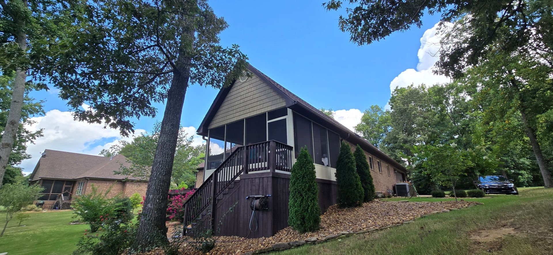 A-frame house with a screened porch surrounded by trees under a blue sky with fluffy clouds.