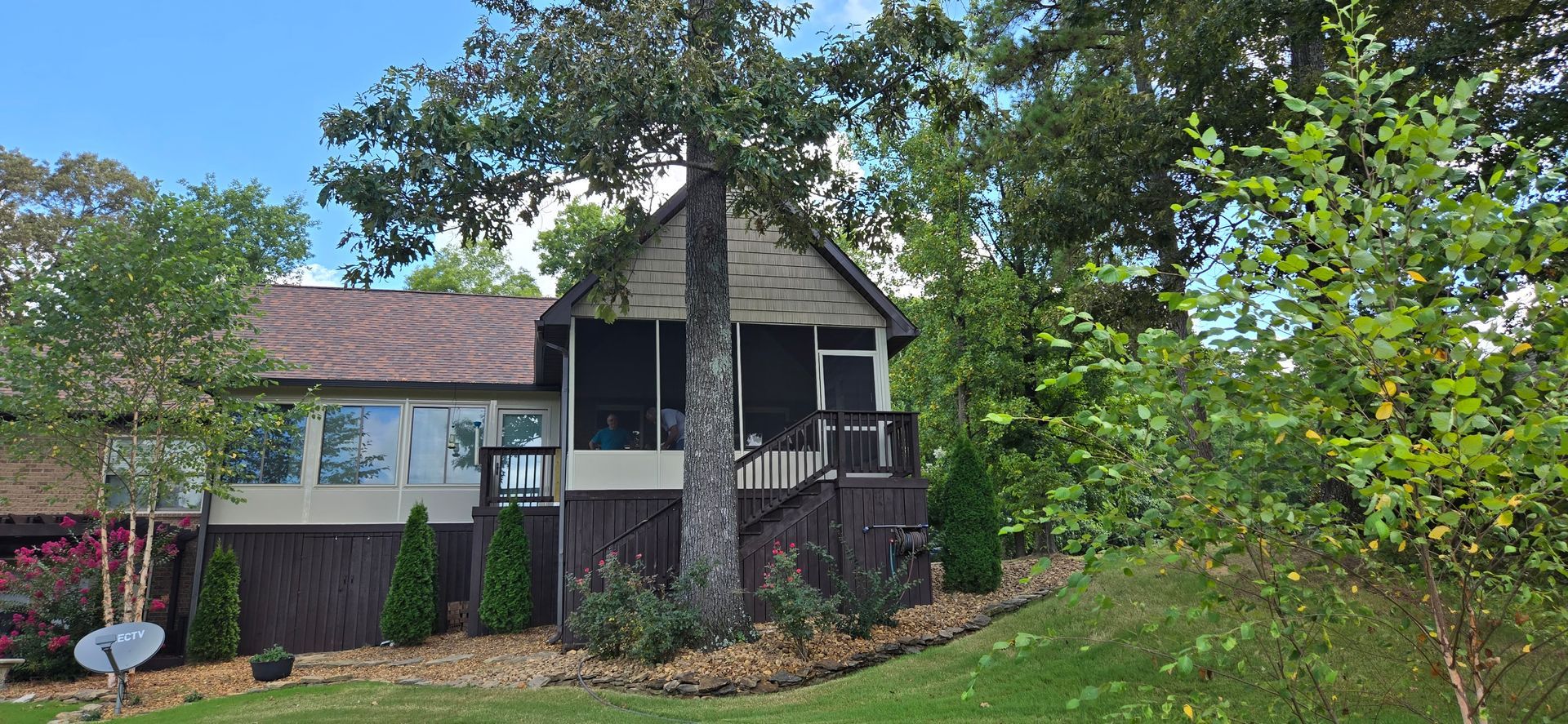 Cabin nestled among trees, with a screened porch and brown siding.