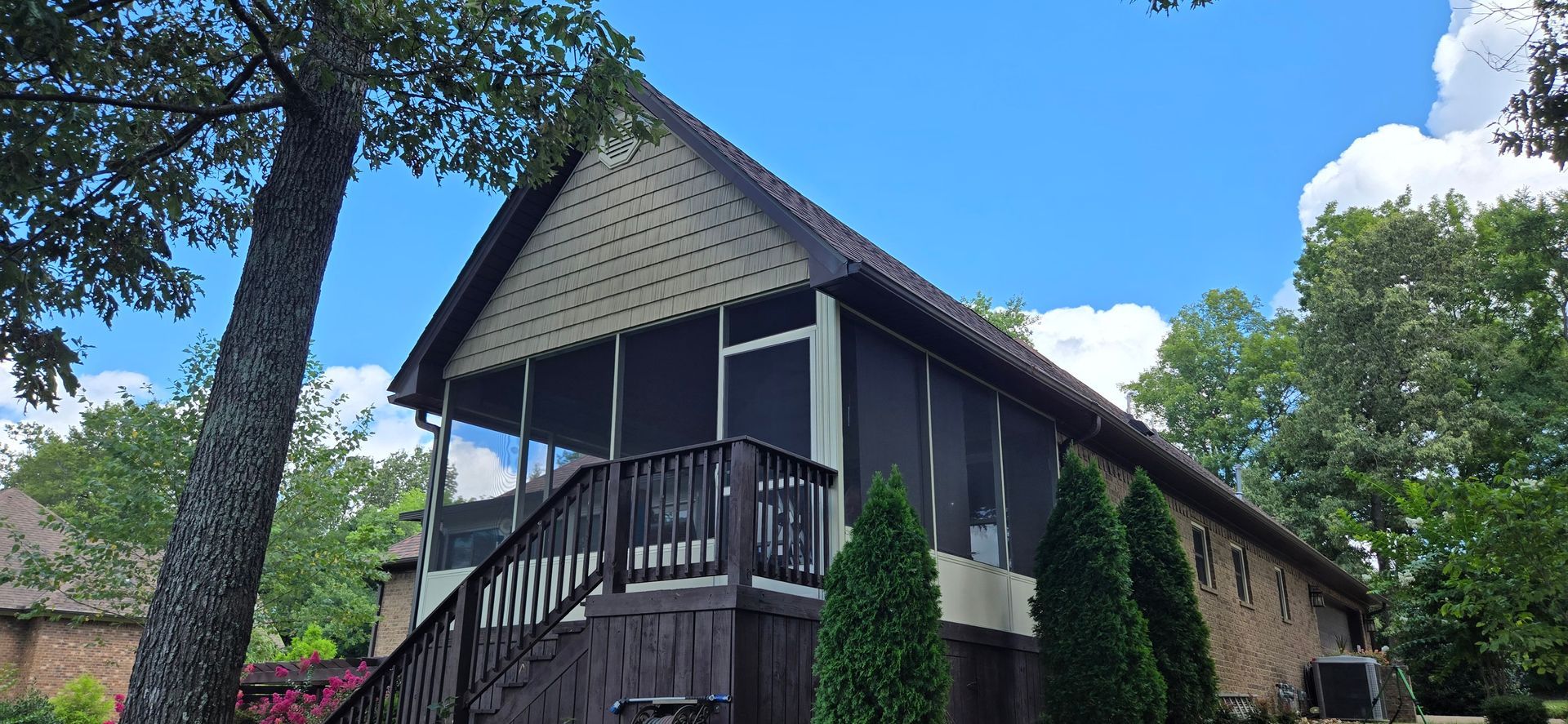 Screened porch with dark trim and roof, under a blue sky. A tree leans in from the left.