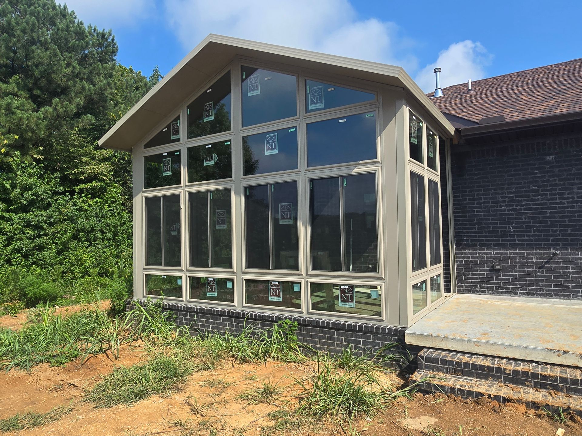 Sunroom addition with large windows, tan trim, attached to a brick home.