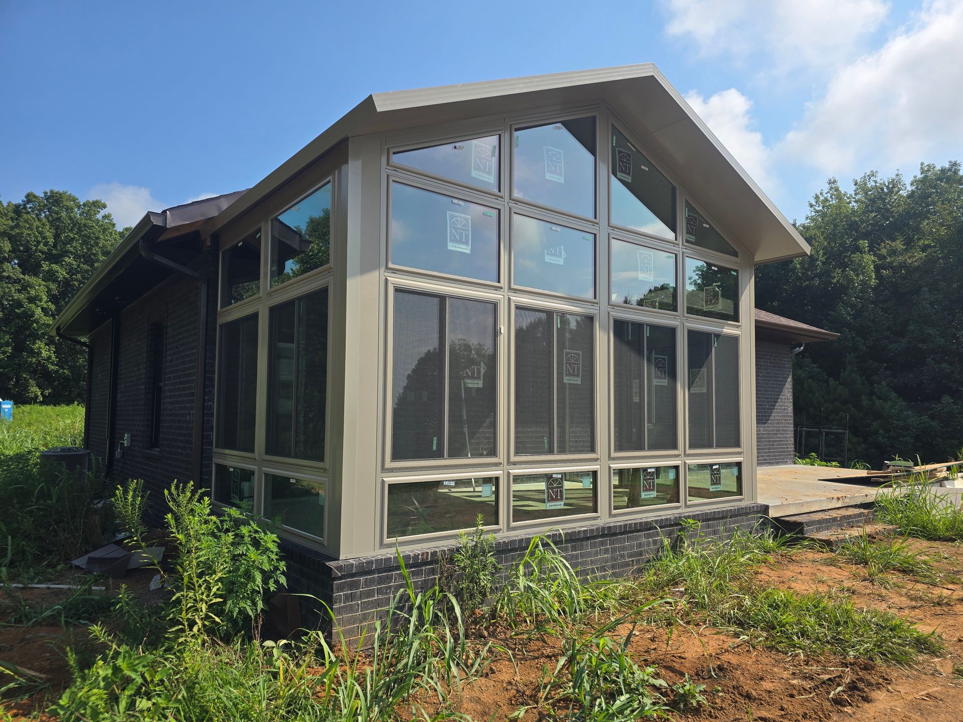 Sunroom addition with large windows on a dark house, surrounded by grass and trees.