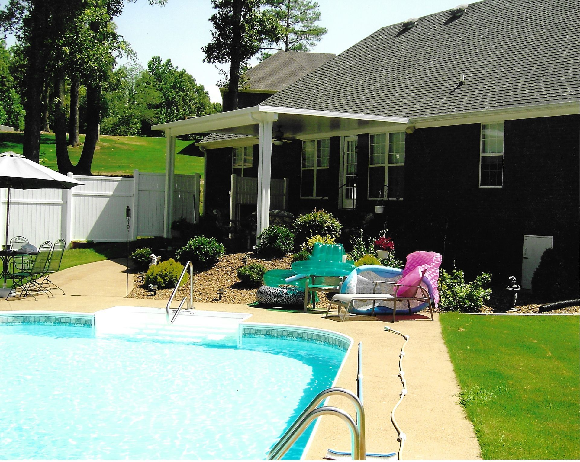 Backyard pool with a house, patio, and lawn on a sunny day.