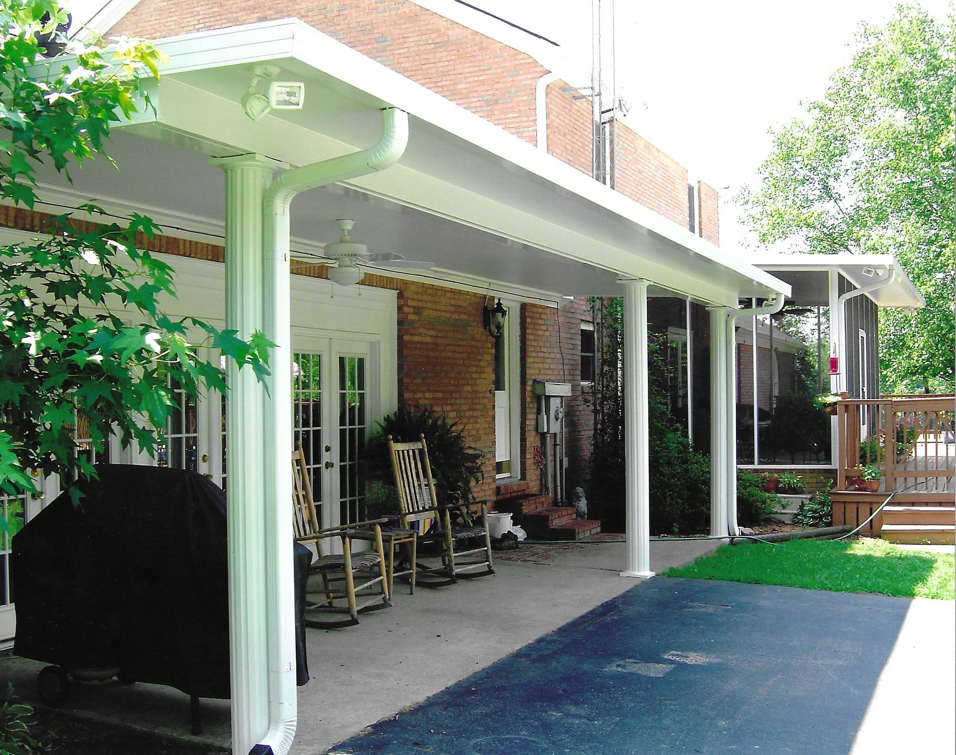 White patio cover attached to a brick home.  Outdoor space with seating, a grill, and a screened-in porch.
