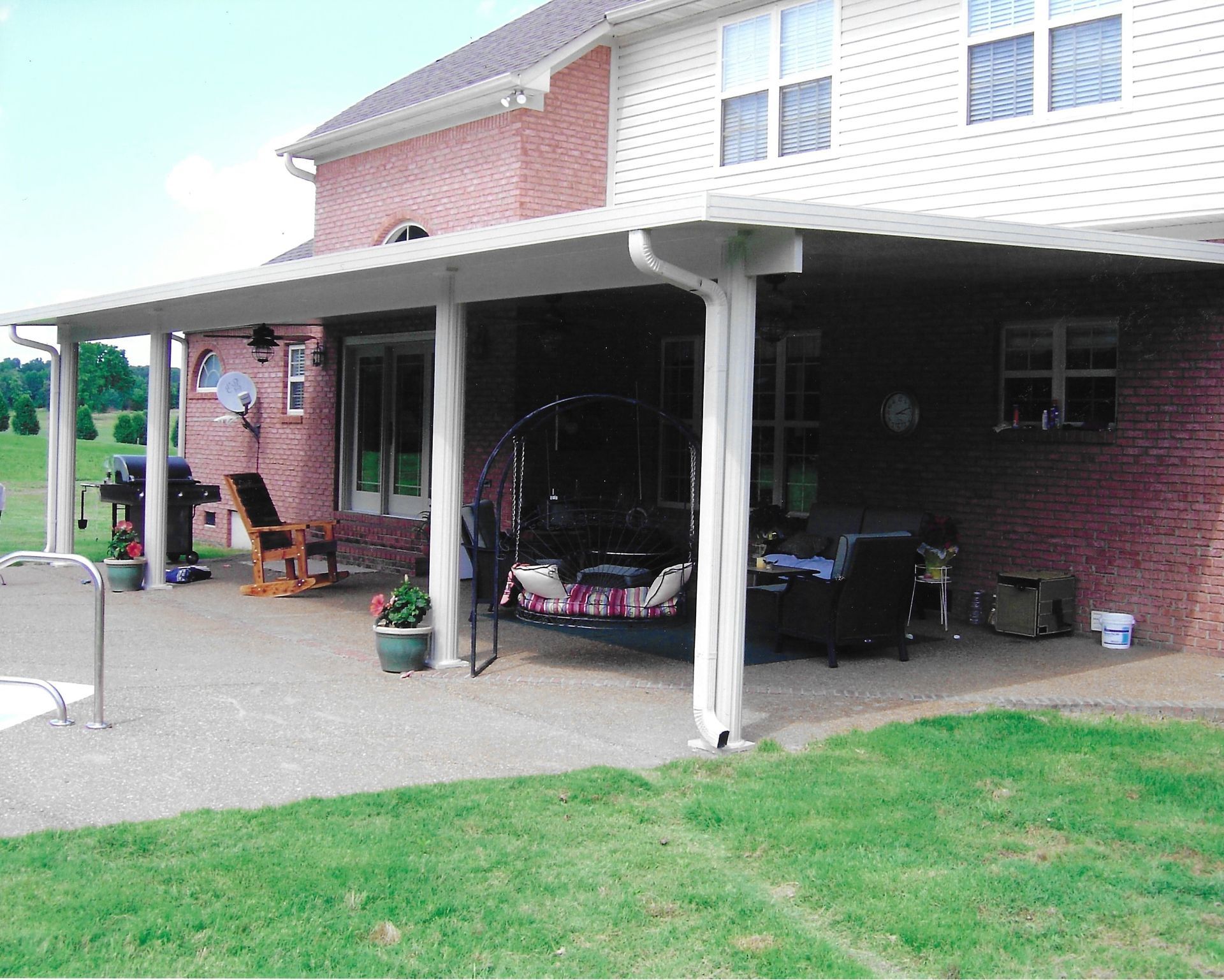 Patio with a white-roofed covering attached to a brick house, featuring outdoor furniture and grass.
