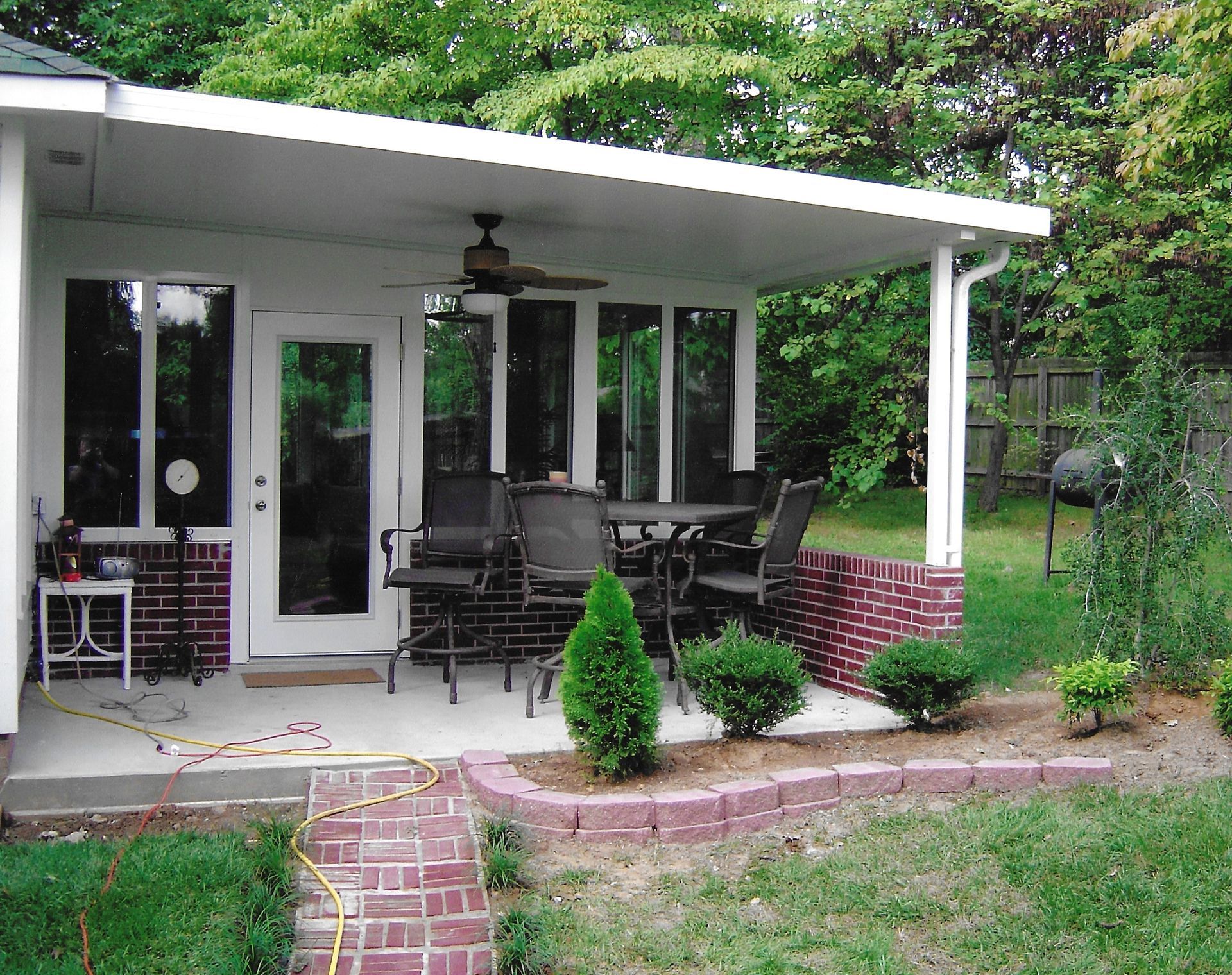 Covered patio with brick accents and outdoor furniture, backed by lush greenery.