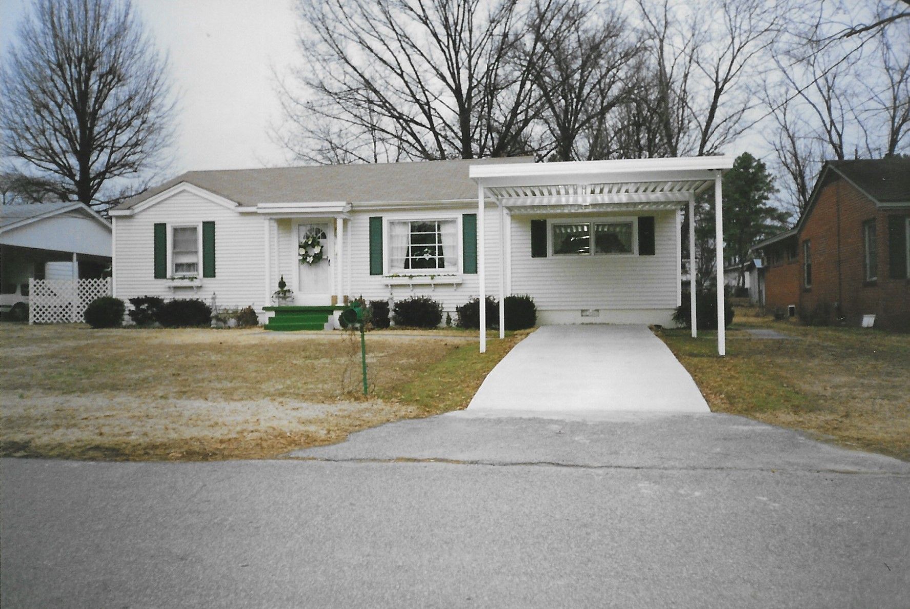 White ranch-style house with green trim, carport, and driveway on a suburban street.