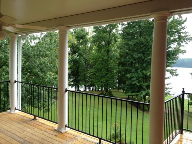 Covered porch with white columns, black railing, and a view of trees and water.
