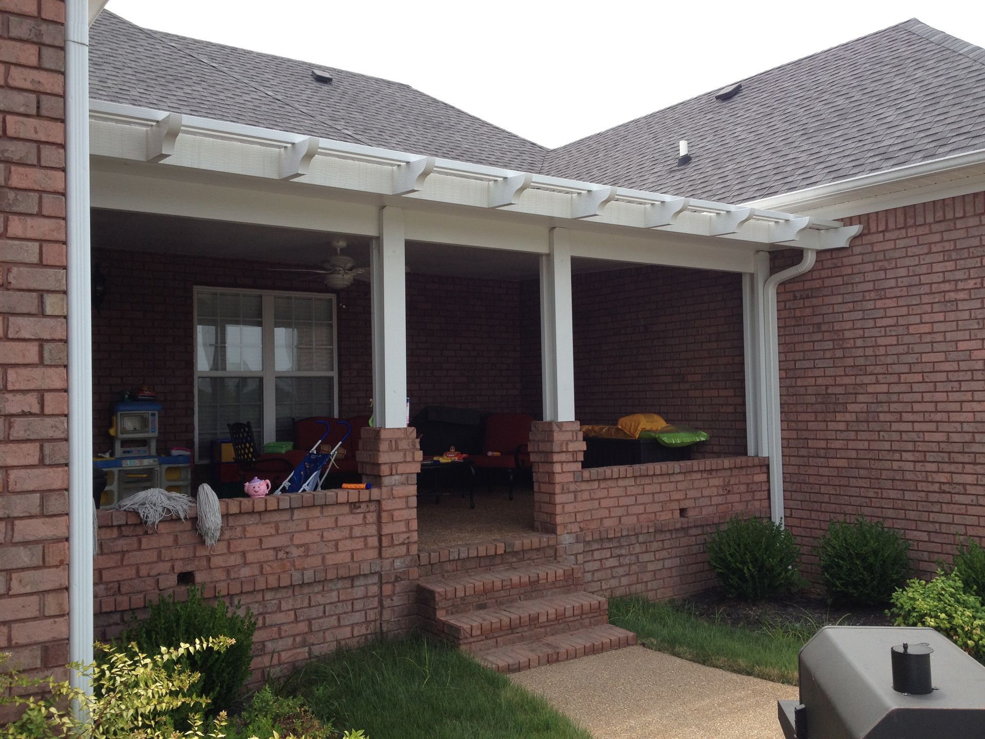 Brick patio with steps, covered by a white pergola, attached to a brick house.
