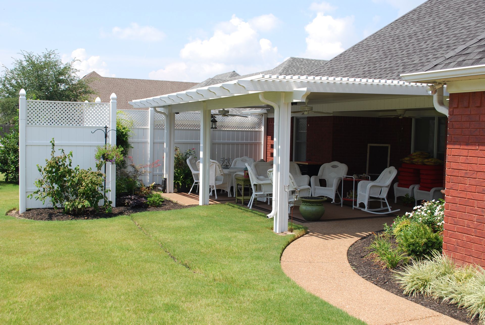 Backyard patio with white pergola, furniture, and lattice fence.