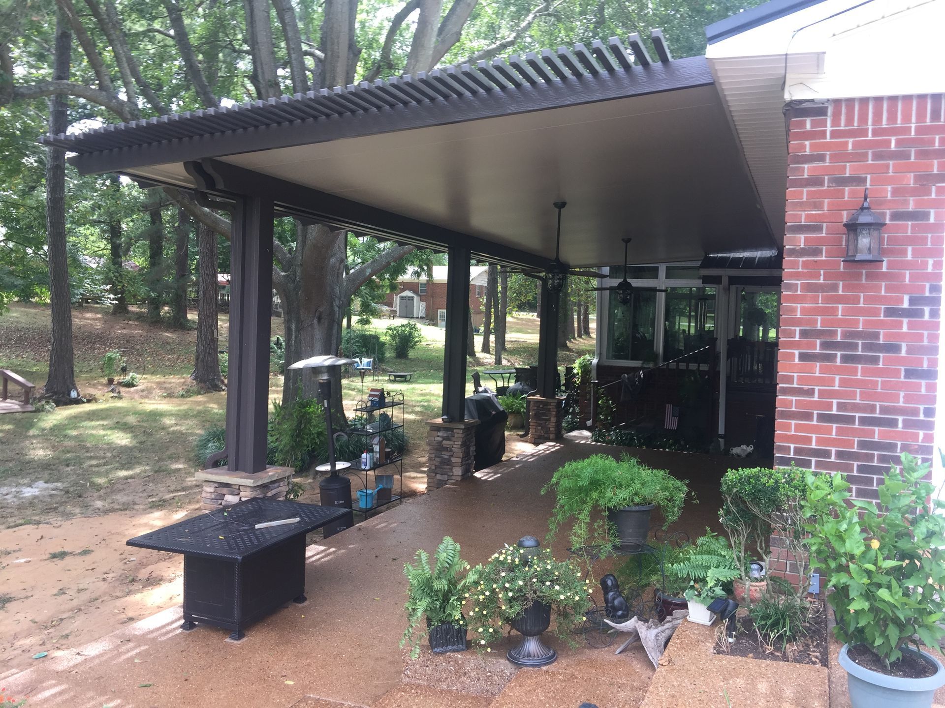 Covered patio with a dark brown structure attached to a brick home.
