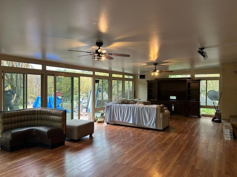Spacious room with wood floors, large windows, ceiling fans, and covered furniture.