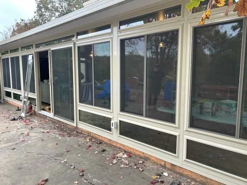 Sunroom exterior with large windows, sliding doors, and a concrete patio with fallen leaves.