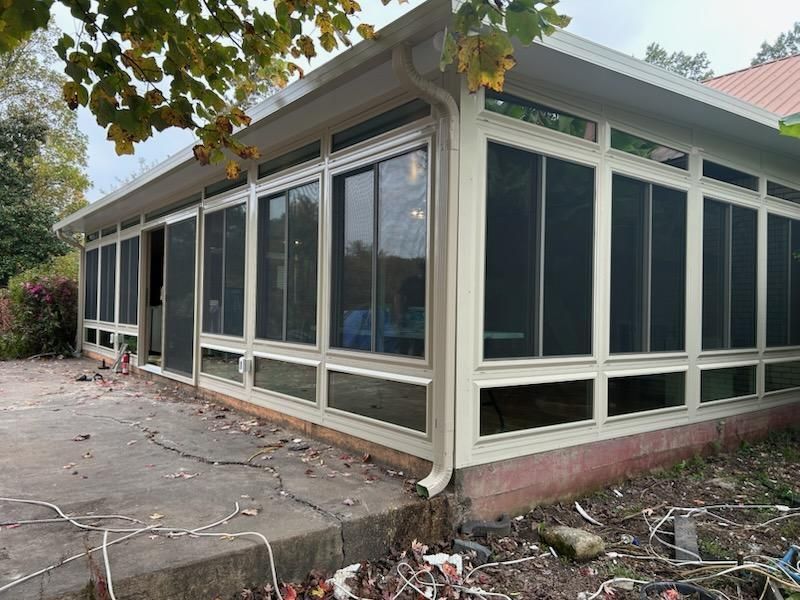 Screened-in porch with multiple windows and a beige frame. Overcast day with leaves on ground.