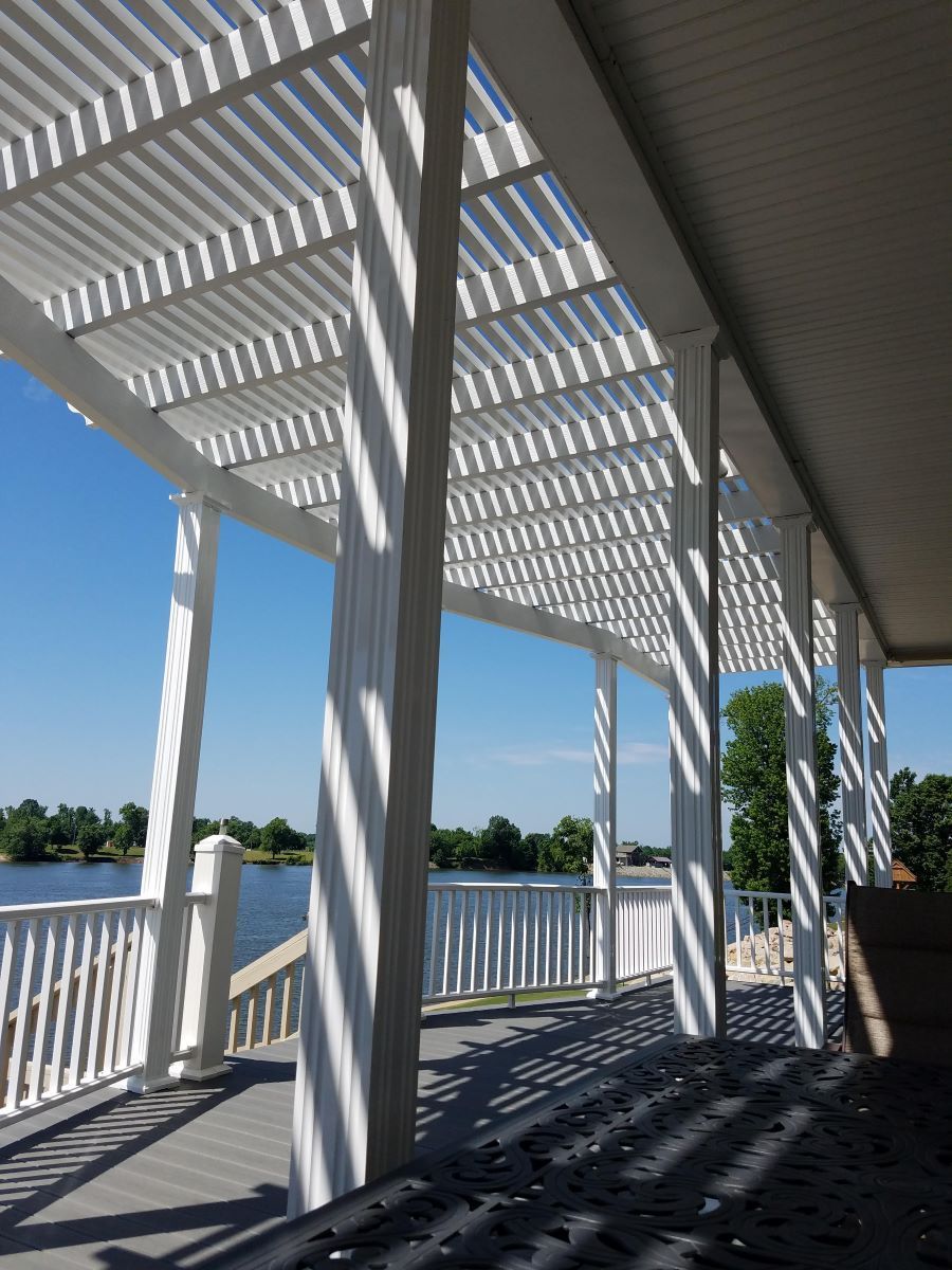 View upwards of a beige and aluminum pergola roof against a blue sky with clouds.