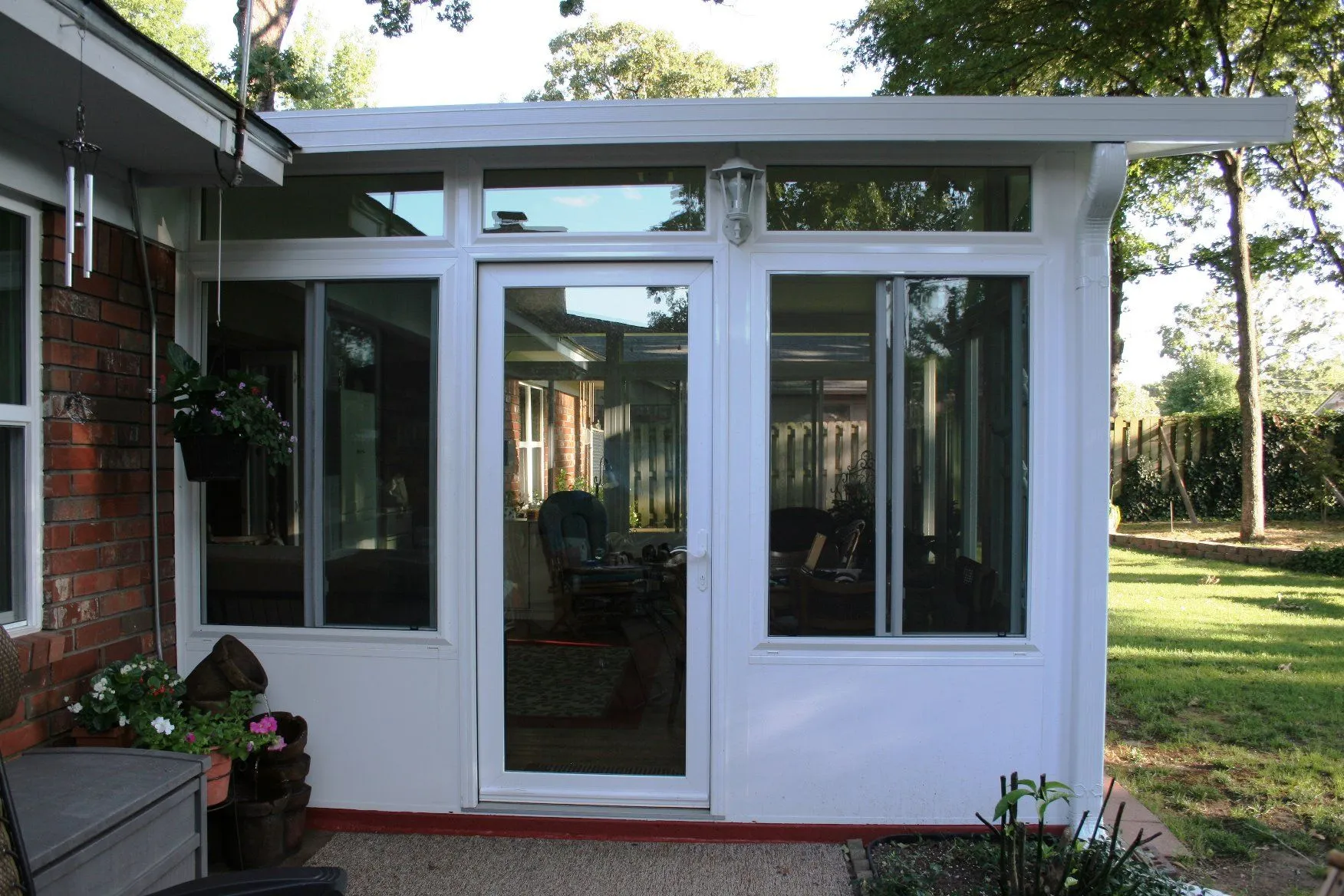 White sunroom addition with glass windows and door, attached to a brick home, overlooking a backyard.