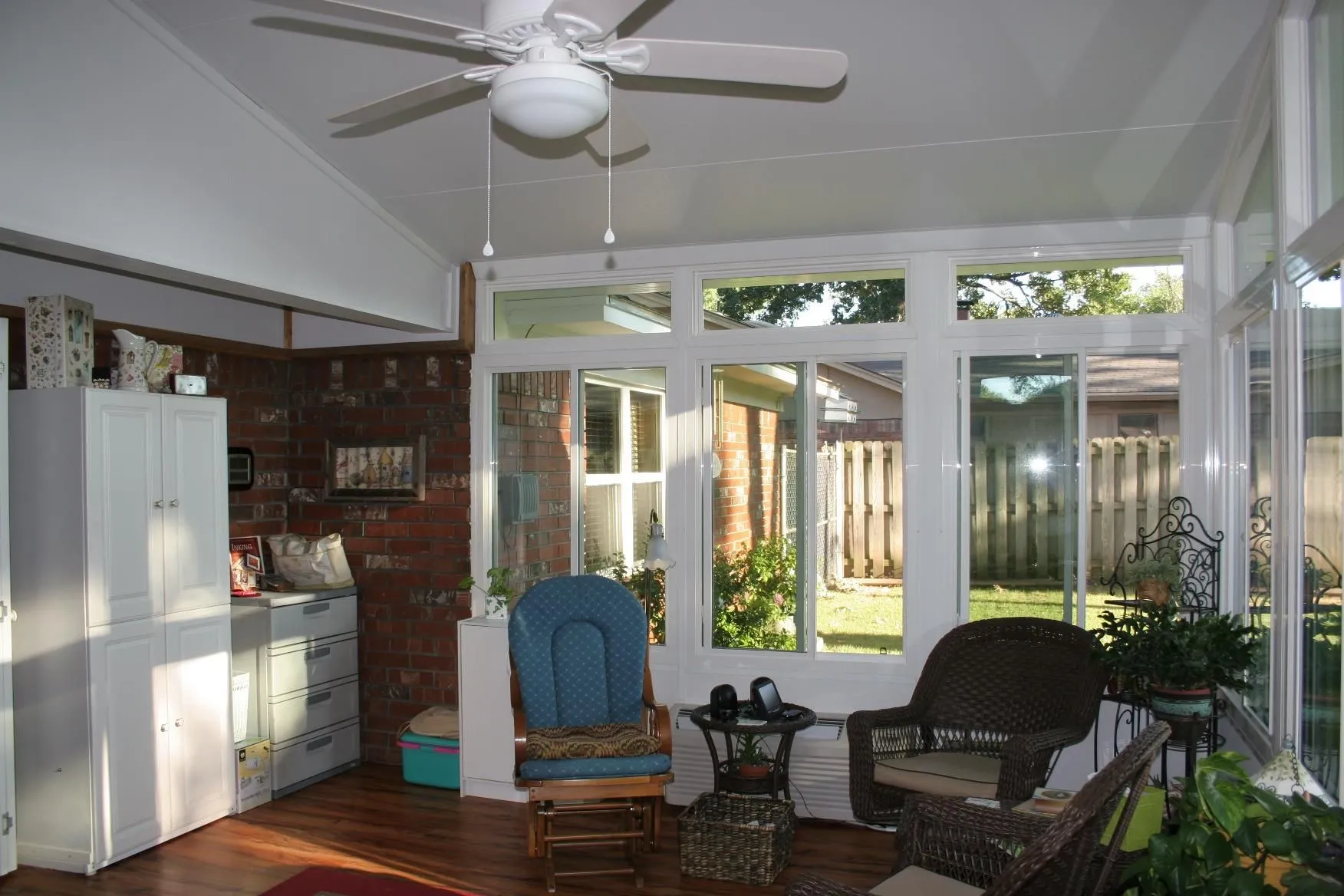 Sunroom with white cabinets, brick wall, wicker furniture, and a view of a backyard.