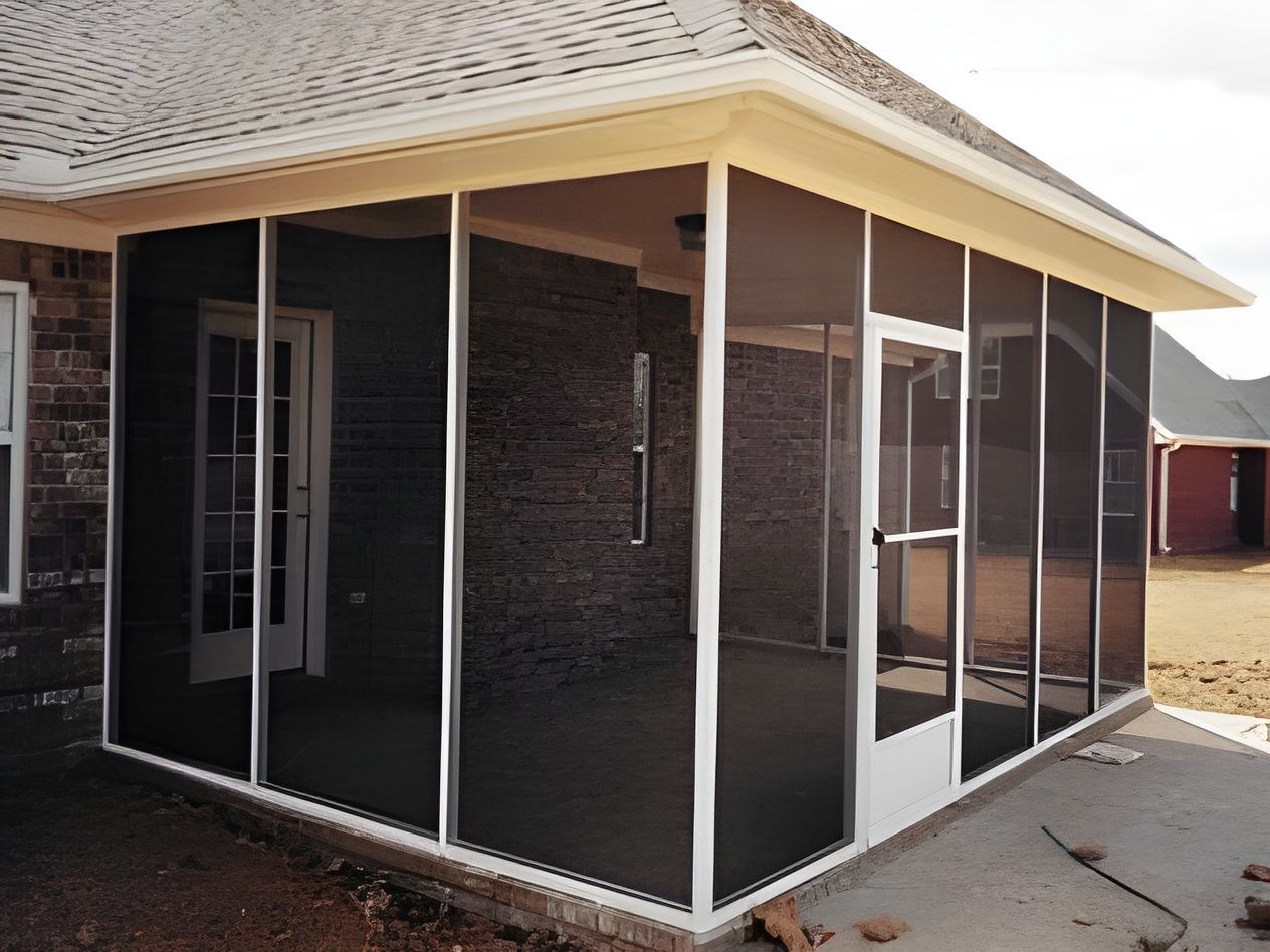 Screened porch with white frame, black screens, and door; adjacent to brick wall.