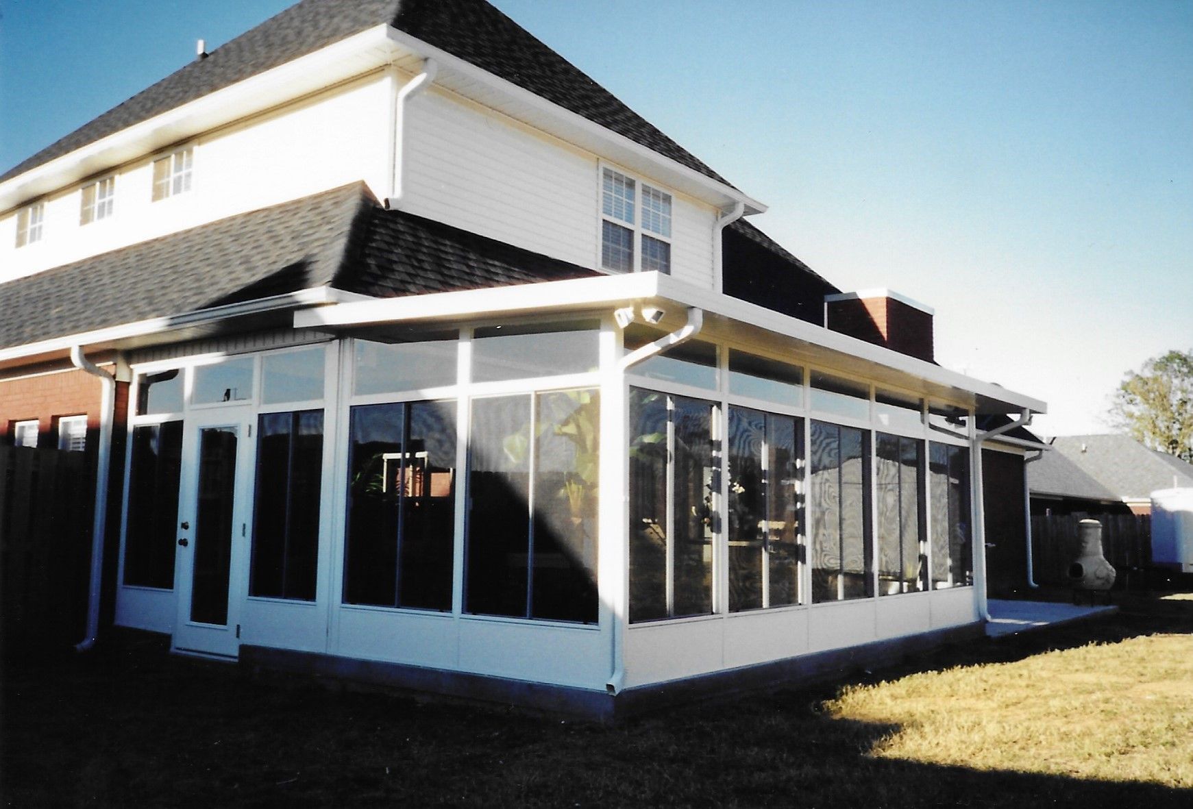 White sunroom attached to a two-story house with dark roof and windows.