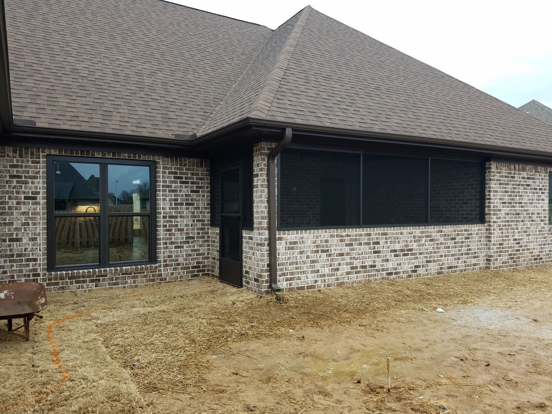 Brick house with dark roof and screened-in porch, set on gravel.
