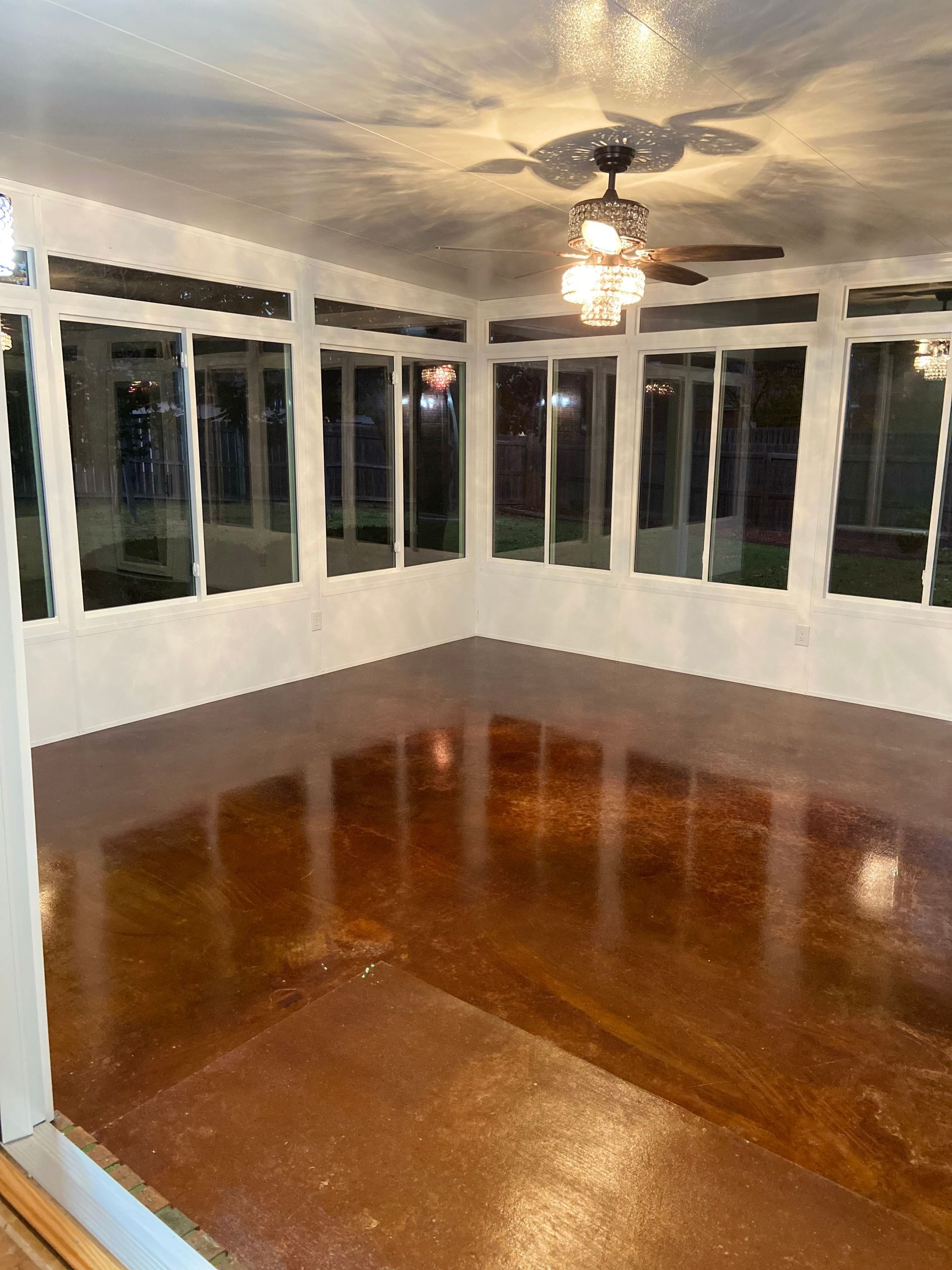 Brown concrete floor sunroom with white trim and windows, a ceiling fan and natural light.