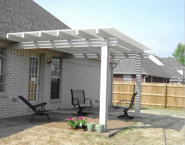 A patio with a pergola and chairs in front of a brick house