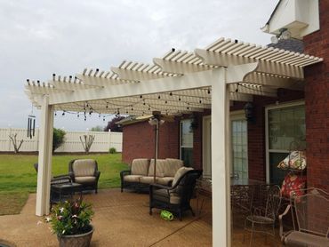 A patio with a pergola and a couch and chairs underneath it