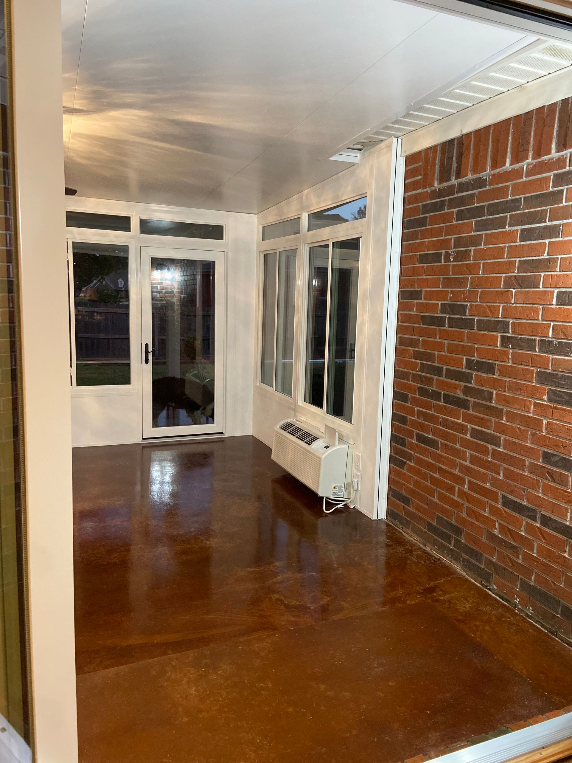 Sunroom with brown floor, brick wall, white trim, and glass doors.