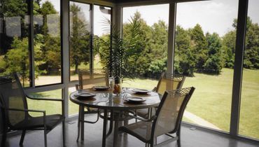 A screened in porch with a table and chairs and a view of trees