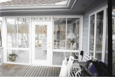 A screened in porch with a lot of windows and chairs