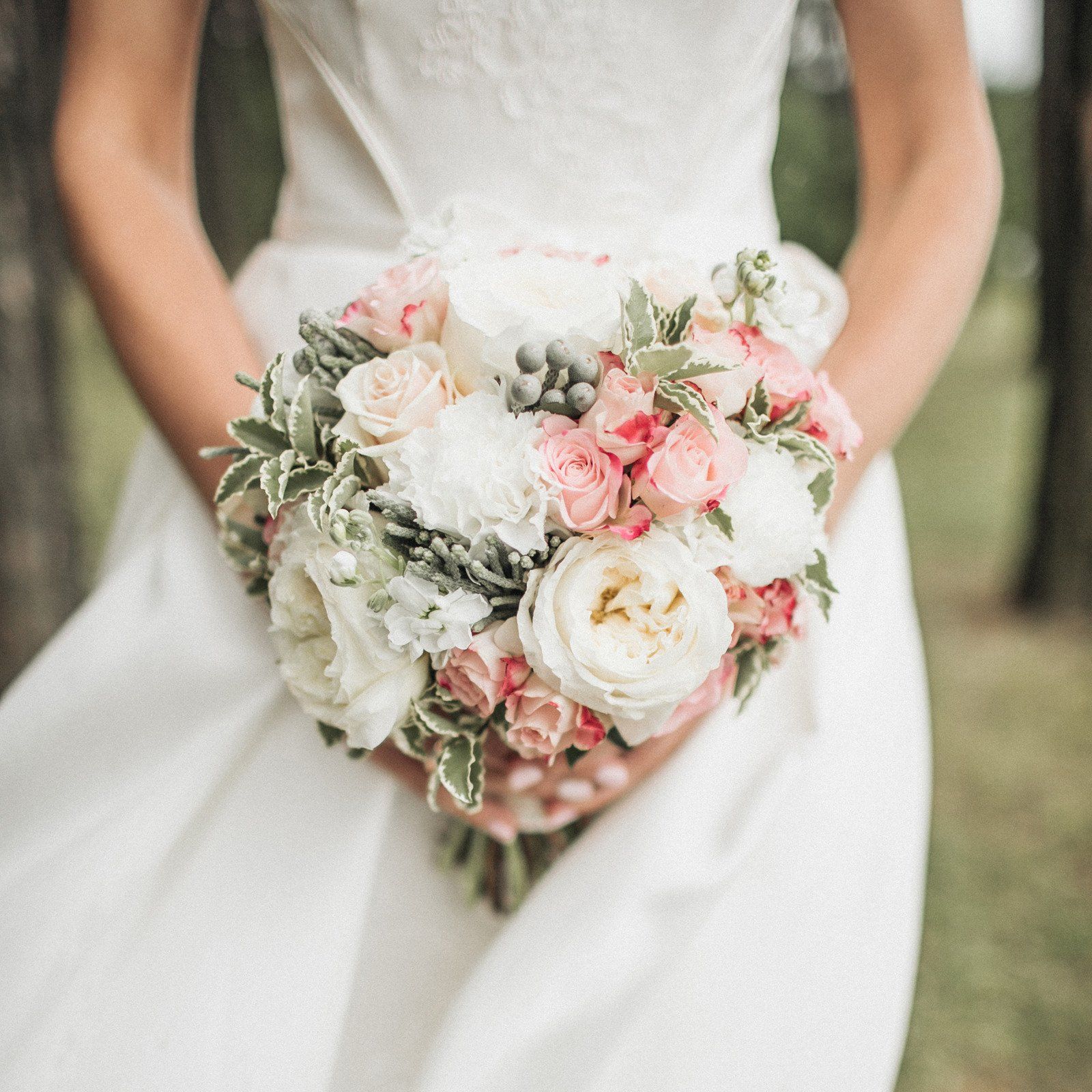 Bride in a white dress holding a bouquet of pink and white flowers, outdoors.