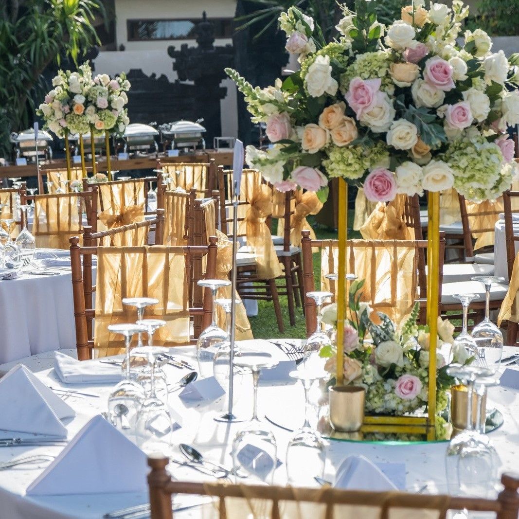 Wedding reception tables set with white linens, gold chairs, and large floral centerpieces.