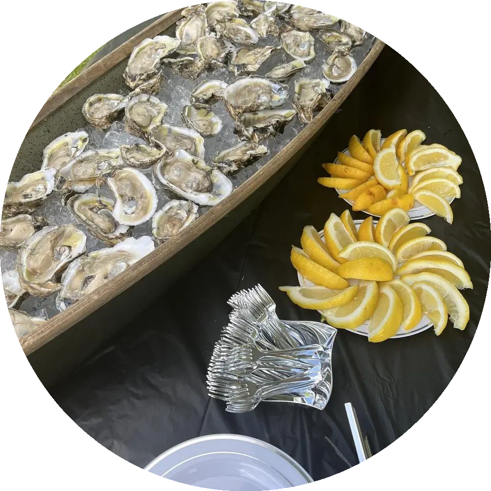 Oysters on ice in a wooden trough, with lemon wedges on plates and forks on a black table.