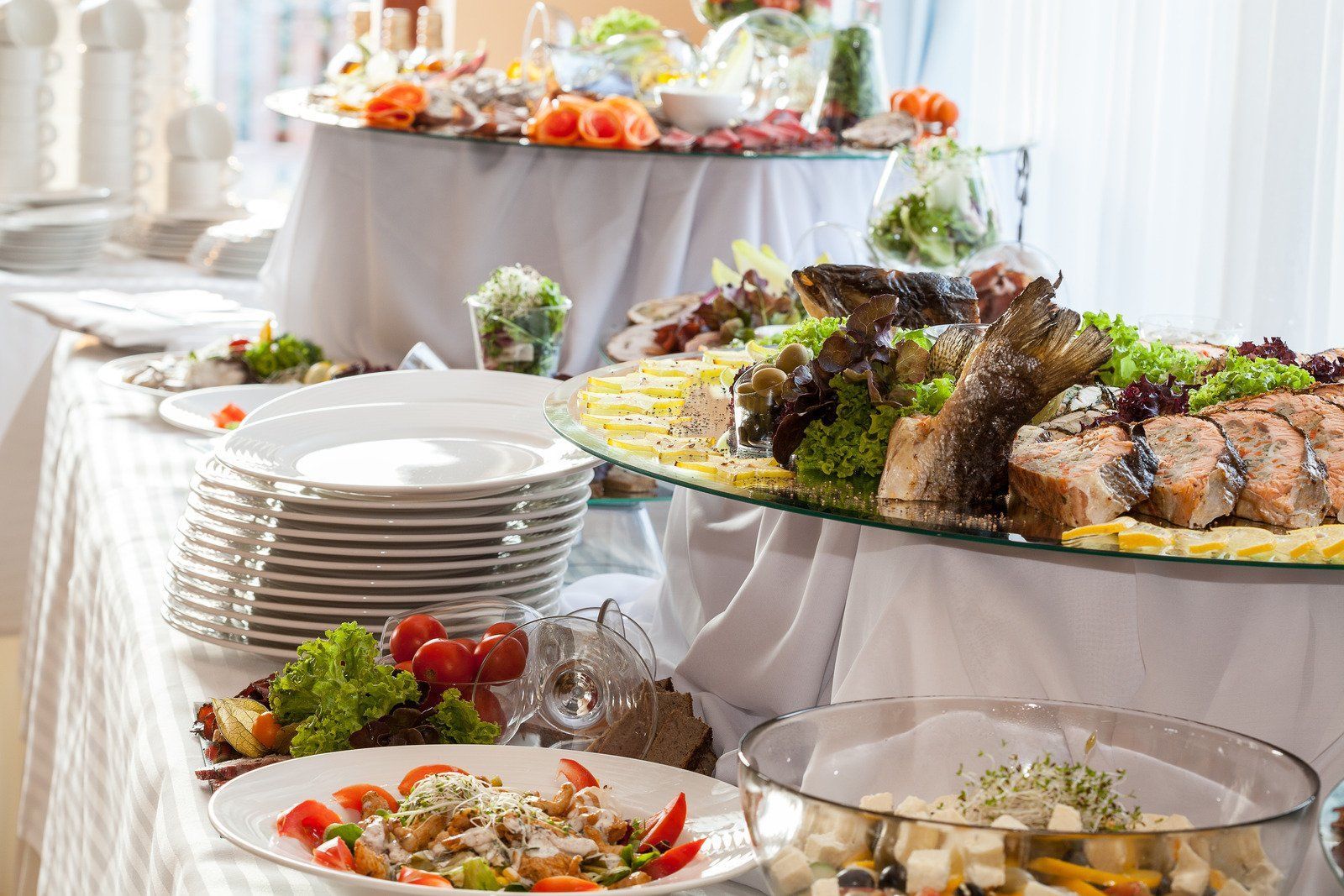 Buffet with various dishes, including fish, salads, and fruits, arranged on tiered tables.