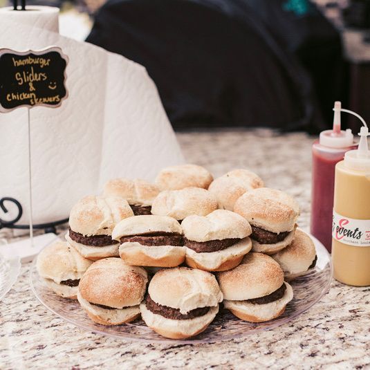 A plate of hamburger sliders with ketchup and mustard on the side, and a chalkboard sign that says 