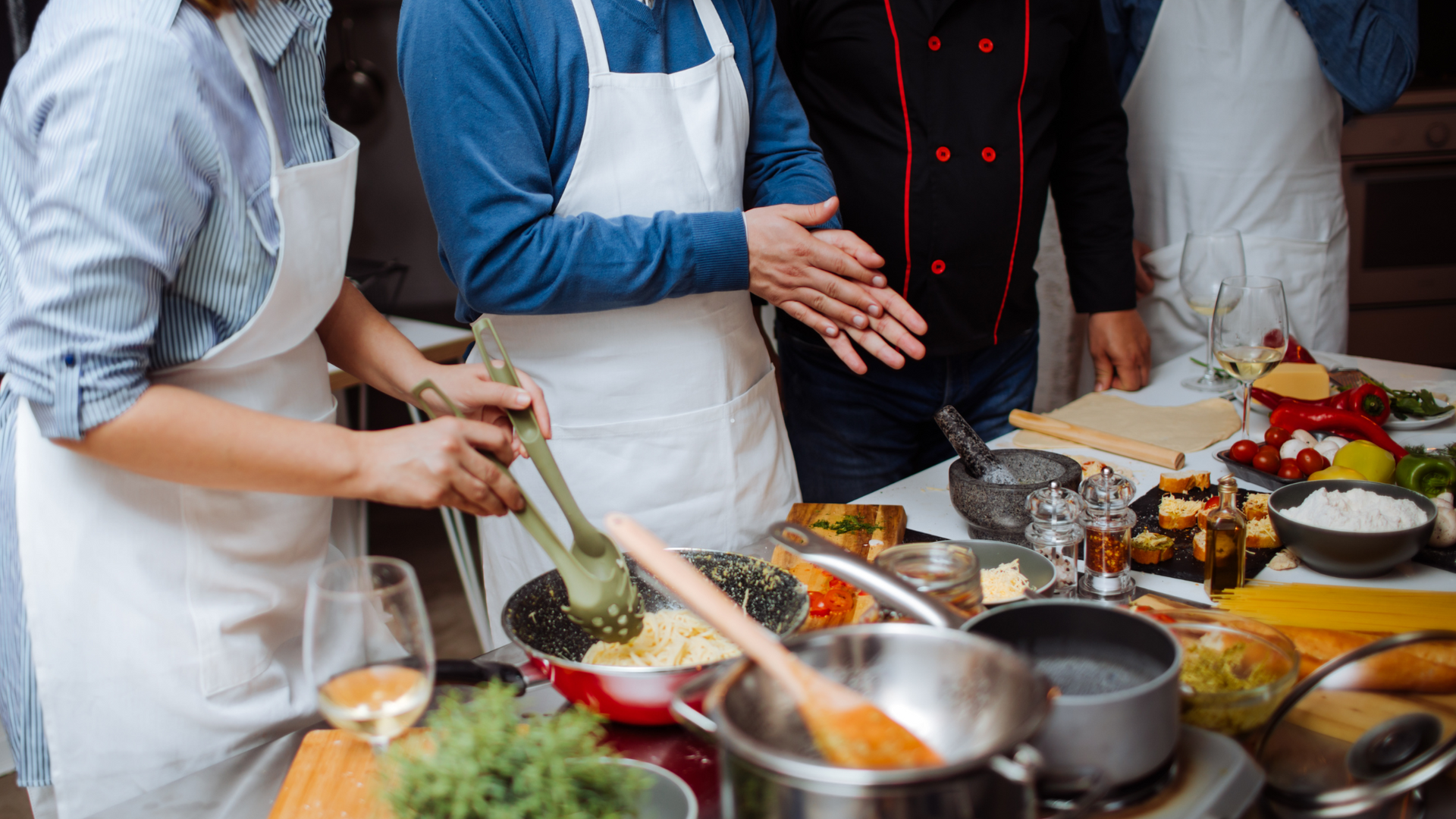 People cooking in a kitchen; chef stirring food in a pan, ingredients on the counter.
