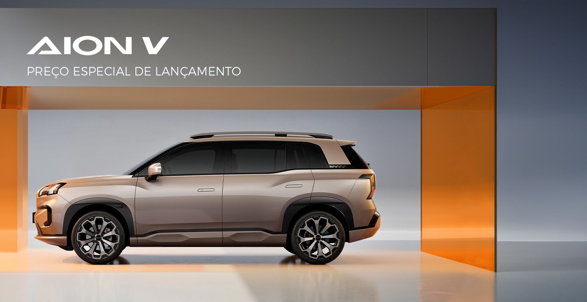 SUV AION V prateado exposto em um showroom elegante com fundo laranja e cinza.