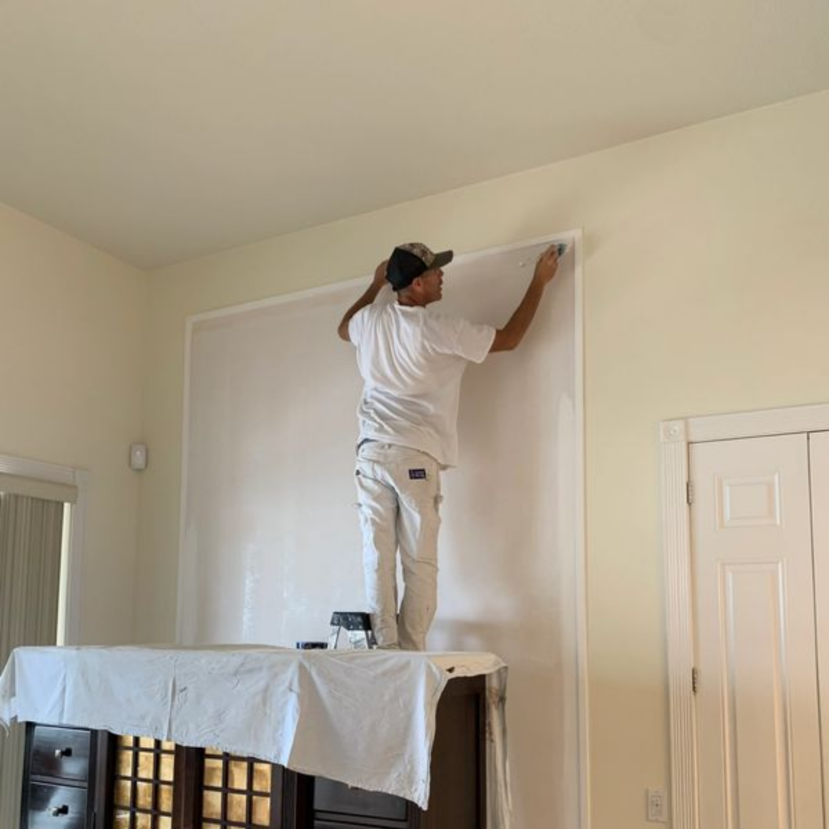 A man is standing on a ladder painting a wall