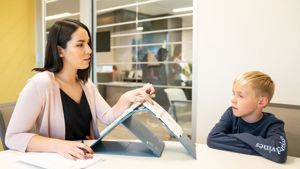 A woman is sitting at a table talking to a young boy.