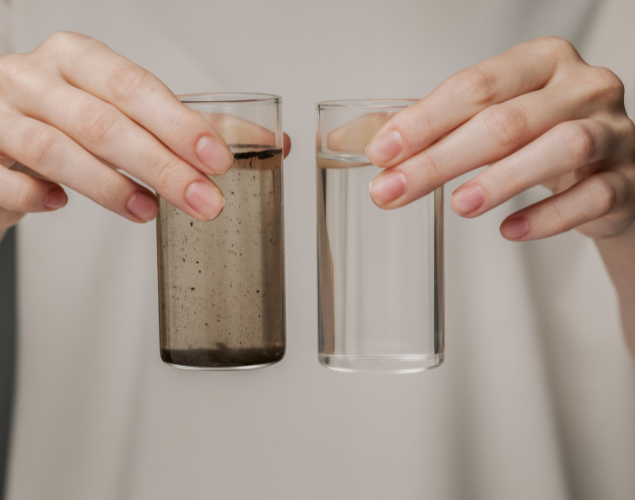 Hands holding two test tubes, one cloudy brown liquid and one clear liquid, against a plain background