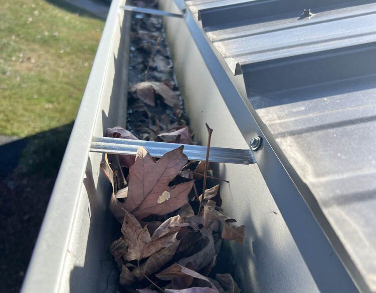 A gutter filled with leaves and dirt on a roof.
